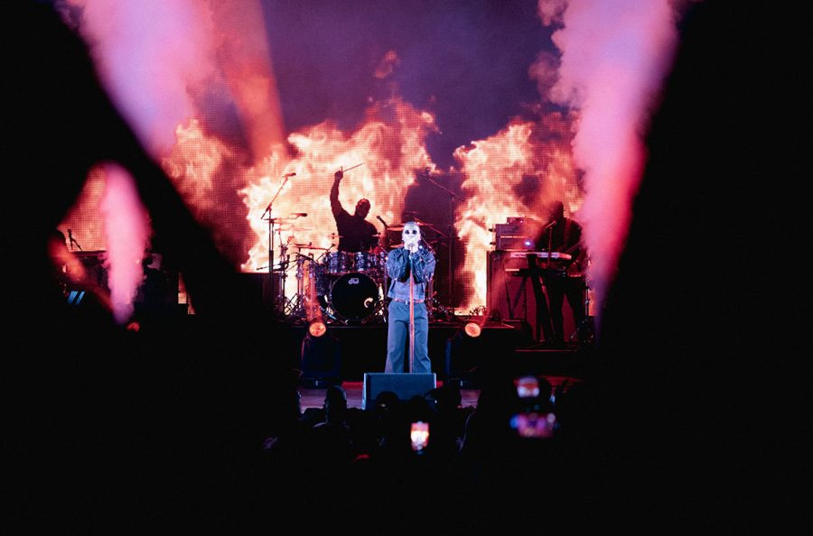 Stage illuminating with purple and pink lighting and fire with singer in the foreground