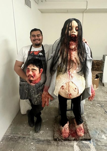 Artist, Carlos Gomez holding a fake sculpted severed head standing next to another monster-like sculpture.